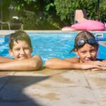 Dwóch chłopców pływa w ogrodowym basenie który ma czystą wodę