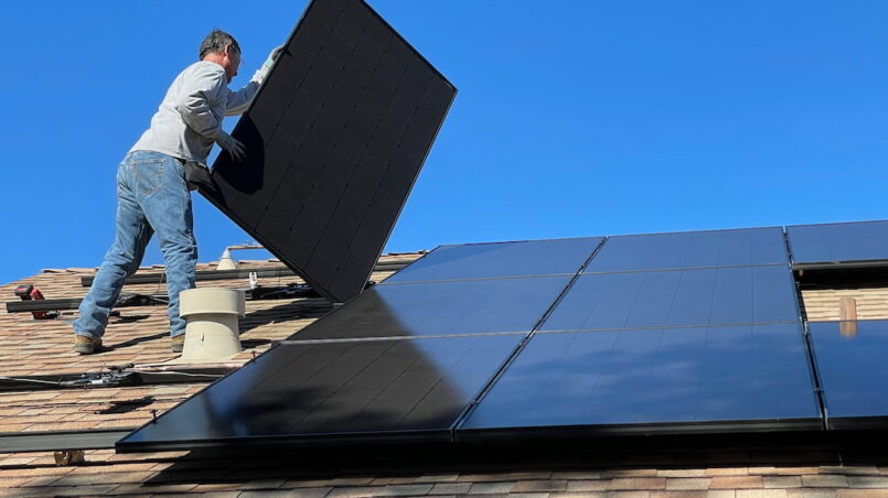 Mężczyzna montuje panele fotowoltaiczne na dachu domu
